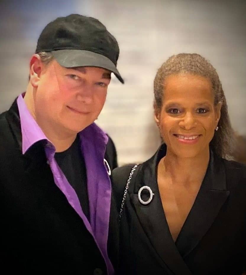 Shepherd Clark and Debi Thomas. Clark is wearing a black baseball cap and a purple collared shirt with a black jacket over top. Thomas (right) is an older Blaxk woman wearing a black blazer